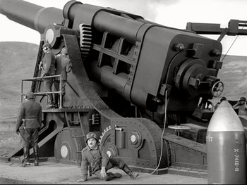 Movie still from “The Great Dictator” (1940), directed by Charles Chaplin – A man sitting on the ground next to a large cannon; Wide shot, Low angle