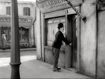 Movie still from “The Great Dictator” (1940), directed by Charles Chaplin – An old photo of a man in a suit and hat opening the door to a barber shop; Wide shot, High angle