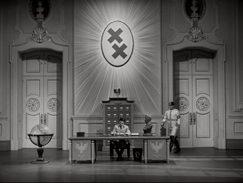 Movie still from “The Great Dictator” (1940), directed by Charles Chaplin – Two men are sitting at a desk in front of a wall with an x on it; Extreme Wide shot, Low angle