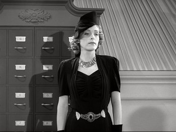 Movie still from “The Great Dictator” (1940), directed by Charles Chaplin – A woman in a black dress wearing a hat and holding her hands behind her back; Medium shot, Low angle