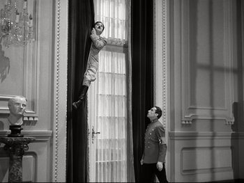 Movie still from “The Great Dictator” (1940), directed by Charles Chaplin – A man hanging from a curtain next to another man; Wide shot, Low angle