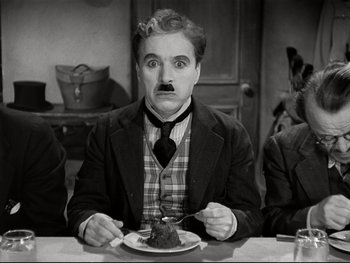 Movie still from “The Great Dictator” (1940), directed by Charles Chaplin – A man with a mustache sitting at a table with a piece of cake in front of him; Medium shot, High angle