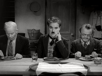 Movie still from “The Great Dictator” (1940), directed by Charles Chaplin – A group of people sitting at a table with plates of food; Medium shot, High angle