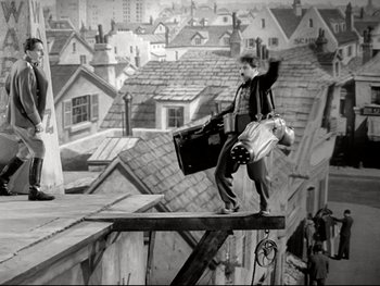 Movie still from “The Great Dictator” (1940), directed by Charles Chaplin – A man standing on top of a building holding luggage; Wide shot, Low angle