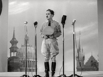 Movie still from “The Great Dictator” (1940), directed by Charles Chaplin – A man standing in front of four microphones in a black and white photo; Wide shot, Low angle