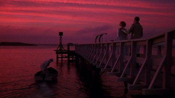 Movie still from “The Great Gatsby” (1974), directed by Jack Clayton – Two people sitting on a pier at sunset; Extreme Wide shot, Low angle