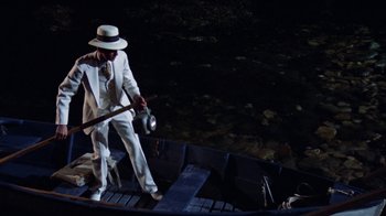 Movie still from “The Great Gatsby” (1974), directed by Jack Clayton – A man in a white suit and hat is standing on a boat; Wide shot, High angle