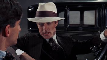 Movie still from “The Great Gatsby” (1974), directed by Jack Clayton – A man in a suit and a hat sitting in front of an antique car; Close Up shot, Over the shoulder angle