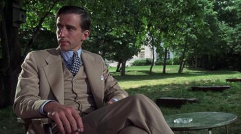 Movie still from “The Great Gatsby” (1974), directed by Jack Clayton – A man sitting on a park bench wearing a suit and tie; Medium shot, Low angle