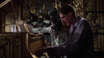 Movie still from “The Great Gatsby” (1974), directed by Jack Clayton – A man playing the piano in front of statues; Medium shot, High angle