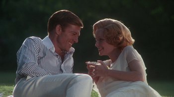 Movie still from “The Great Gatsby” (1974), directed by Jack Clayton – A man and a woman sitting next to each other on the grass; Medium shot, Low angle