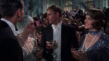 Movie still from “The Great Gatsby” (1974), directed by Jack Clayton – A group of people standing around each other holding wine glasses; Medium shot, Low angle