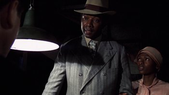 Movie still from “The Great Gatsby” (1974), directed by Jack Clayton – A man in a suit and hat standing in a dimly lit room; Close Up shot, Low angle