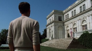 Movie still from “The Great Gatsby” (1974), directed by Jack Clayton – A man standing in front of a large white building; Wide shot, Low angle