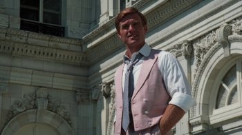 Movie still from “The Great Gatsby” (1974), directed by Jack Clayton – A man in a suit and tie standing in front of a building; Medium shot, Low angle