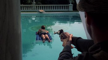 Movie still from “The Great Gatsby” (1974), directed by Jack Clayton – A man taking a picture of a man laying on a raft in a pool; Wide shot, High angle