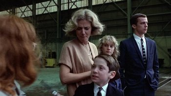 Movie still from “The Great Santini” (1979), directed by Lewis John Carlino – A woman and two children are standing in an industrial setting; Medium shot, Over the shoulder angle