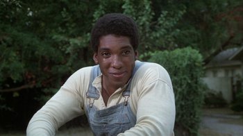 Movie still from “The Great Santini” (1979), directed by Lewis John Carlino – A young man in overalls sitting in front of trees; Close Up shot, High angle