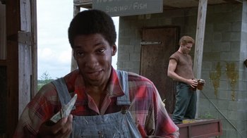 Movie still from “The Great Santini” (1979), directed by Lewis John Carlino – A man in a plaid shirt holding money in front of a brick building; Medium shot, Low angle