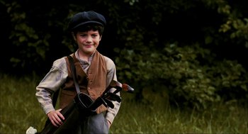 Movie still from “The Greatest Game Ever Played” (2005), directed by Bill Paxton – A young boy holding a pair of golf clubs in his hands; Medium shot, High angle