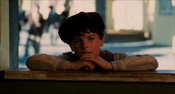 Movie still from “The Greatest Game Ever Played” (2005), directed by Bill Paxton – A young boy wearing a black hat leaning against a wall; Close Up shot, High angle