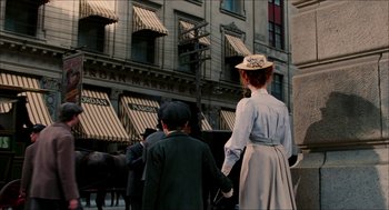 Movie still from “The Greatest Game Ever Played” (2005), directed by Bill Paxton – A woman and a boy are riding in a horse drawn carriage down the street; Wide shot, Over the shoulder angle