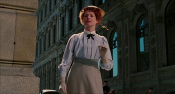Movie still from “The Greatest Game Ever Played” (2005), directed by Bill Paxton – A woman in a hat and gloves standing in front of a building; Medium shot, Low angle
