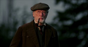 Movie still from “The Greatest Game Ever Played” (2005), directed by Bill Paxton – An older man wearing a hat and smoking a pipe; Close Up shot, Low angle