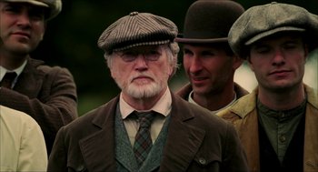 Movie still from “The Greatest Game Ever Played” (2005), directed by Bill Paxton – An older man wearing a hat and a tie; Medium shot, Over the shoulder angle