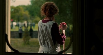 Movie still from “The Greatest Game Ever Played” (2005), directed by Bill Paxton – A woman standing in front of a window holding a cane; Medium shot, Over the shoulder angle