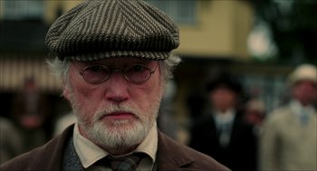Movie still from “The Greatest Game Ever Played” (2005), directed by Bill Paxton – An older man wearing a hat , glasses and a suit; Close Up shot, Low angle