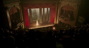 Movie still from “The Greatest Game Ever Played” (2005), directed by Bill Paxton – A woman in white stands on a stage in front of a crowd; Extreme Wide shot, High angle