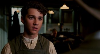 Movie still from “The Greatest Game Ever Played” (2005), directed by Bill Paxton – A young man wearing an apron in a room; Close Up shot, Over the shoulder angle