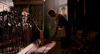 Movie still from “The Greatest Game Ever Played” (2005), directed by Bill Paxton – A man in an apron is looking at golf clubs in a store; Medium shot, Low angle