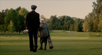 Movie still from “The Greatest Game Ever Played” (2005), directed by Bill Paxton – Two men walking on a lush green field with trees in the background; Wide shot, Low angle