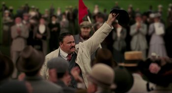 Movie still from “The Greatest Game Ever Played” (2005), directed by Bill Paxton – A man holding a hat up in the air in front of a group of people; Medium shot, Low angle