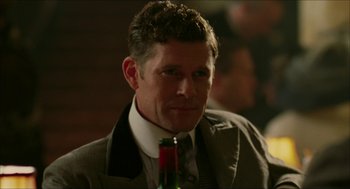 Movie still from “The Greatest Game Ever Played” (2005), directed by Bill Paxton – A person wearing a suit and holding a bottle; Close Up shot, Over the shoulder angle