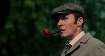 Movie still from “The Greatest Game Ever Played” (2005), directed by Bill Paxton – A man wearing a suit and hat with a pipe in his mouth; Close Up shot, Low angle
