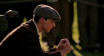 Movie still from “The Greatest Game Ever Played” (2005), directed by Bill Paxton – A man in a hat and a brown jacket looking at his cell phone; Close Up shot, Over the shoulder angle