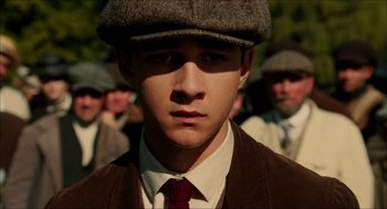 Movie still from “The Greatest Game Ever Played” (2005), directed by Bill Paxton – A young man wearing a hat and a tie in front of a group of men; Close Up shot, Low angle
