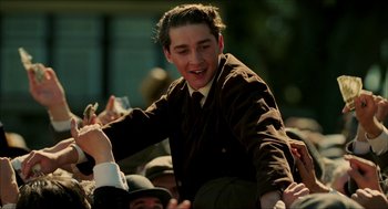 Movie still from “The Greatest Game Ever Played” (2005), directed by Bill Paxton – A man in a suit and tie is sitting in a crowd of people; Medium shot, Low angle