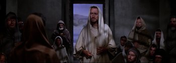 Movie still from “The Greatest Story Ever Told” (1965), directed by David Lean – A man dressed as jesus is standing in front of a group of people; Medium shot, Over the shoulder angle