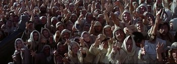 Movie still from “The Greatest Story Ever Told” (1965), directed by David Lean – A large group of people wearing hoods and giving the peace sign; Wide shot, High angle