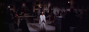 Movie still from “The Greatest Story Ever Told” (1965), directed by David Lean – A group of people sitting in a room with a man in a white robe; Wide shot, High angle