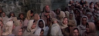 Movie still from “The Greatest Story Ever Told” (1965), directed by David Lean – A group of men and women gathered around a man holding a stick; Medium shot, High angle