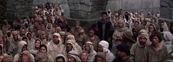 Movie still from “The Greatest Story Ever Told” (1965), directed by David Lean – A group of men standing next to each other in front of a stone wall; Wide shot, High angle