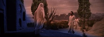 Movie still from “The Greatest Story Ever Told” (1965), directed by David Lean – Two men in robes stand near a tree and a hill; Wide shot, Over the shoulder angle