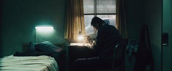 Movie still from “The Grey” (2011), directed by Joe Carnahan – A man sitting at a desk in a room; Medium shot, Low angle