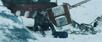 Movie still from “The Grey” (2011), directed by Joe Carnahan – A man sitting in the snow next to an oven; Wide shot, High angle