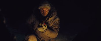 Movie still from “The Grey” (2011), directed by Joe Carnahan – A man wearing a winter coat and a hat is holding a flashlight; Medium shot, Low angle